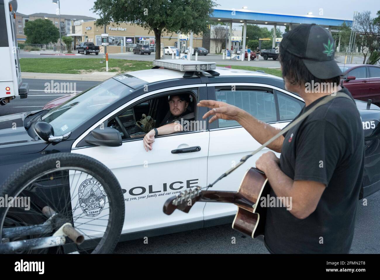 Il musicista e handyman Douglas Crawford saluta un ufficiale della polizia di Austin mentre strums la sua chitarra per il cambio di riserva vicino al suo campo all'angolo di ben White Blvd. E South Congress Avenue ad Austin, TX, dove ha vissuto per oltre un anno. Crawford, 60 anni, dice di rimanere a se stesso e non è preoccupato per il nuovo schiacco senza tetto di Austin e il divieto di campeggio a partire da martedì. ©Bob Daemmrich Foto Stock