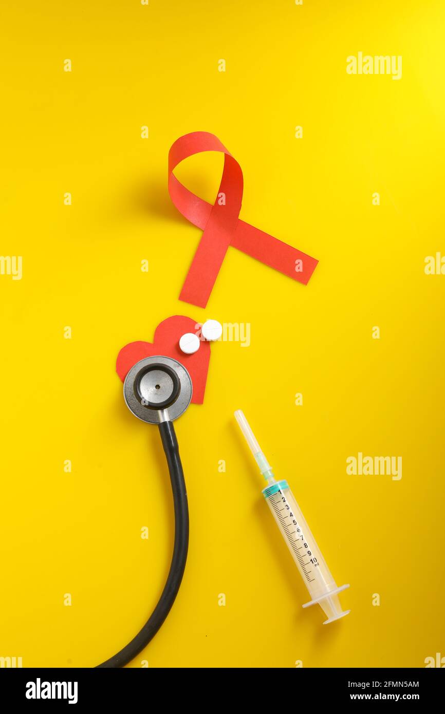 Posto di lavoro del medico con stetoscopio, compresse in blister, siringa su sfondo giallo. Foto Stock