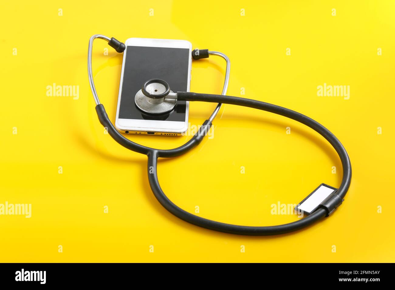 Smartphone e stetoscopio su sfondo giallo. Tecnologia di medicina online (telemedicina). Servizio di diagnostica remota, chat con il medico. Foto Stock