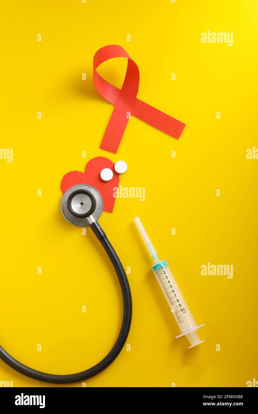 Posto di lavoro del medico con stetoscopio, compresse in blister, siringa su sfondo giallo. Foto Stock