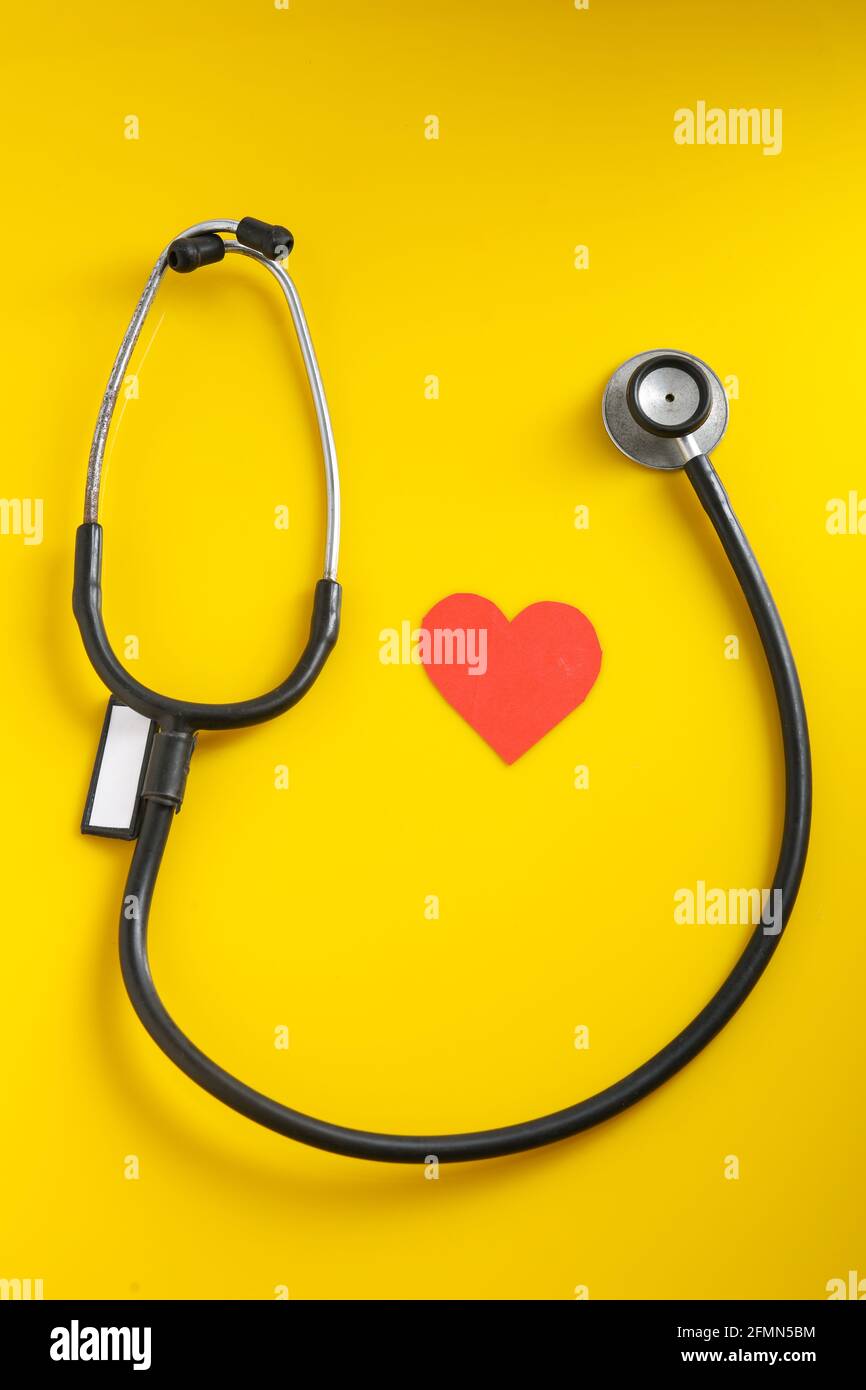 Un cuore con uno stetoscopio su sfondo giallo. Foto Stock