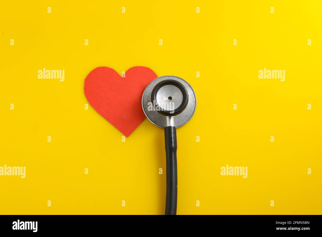 Un cuore con uno stetoscopio su sfondo giallo. Foto Stock