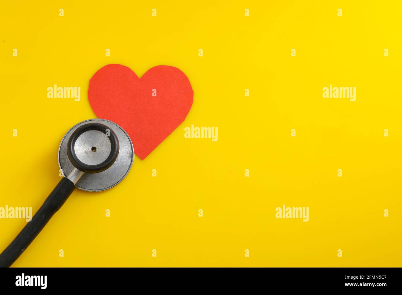 Un cuore con uno stetoscopio su sfondo giallo. Foto Stock