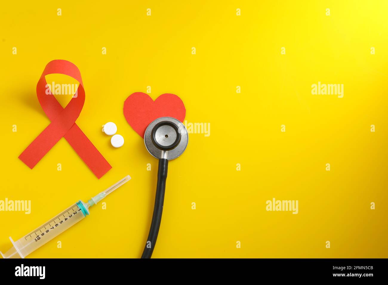 Posto di lavoro del medico con stetoscopio, compresse in blister, siringa su sfondo giallo. Foto Stock