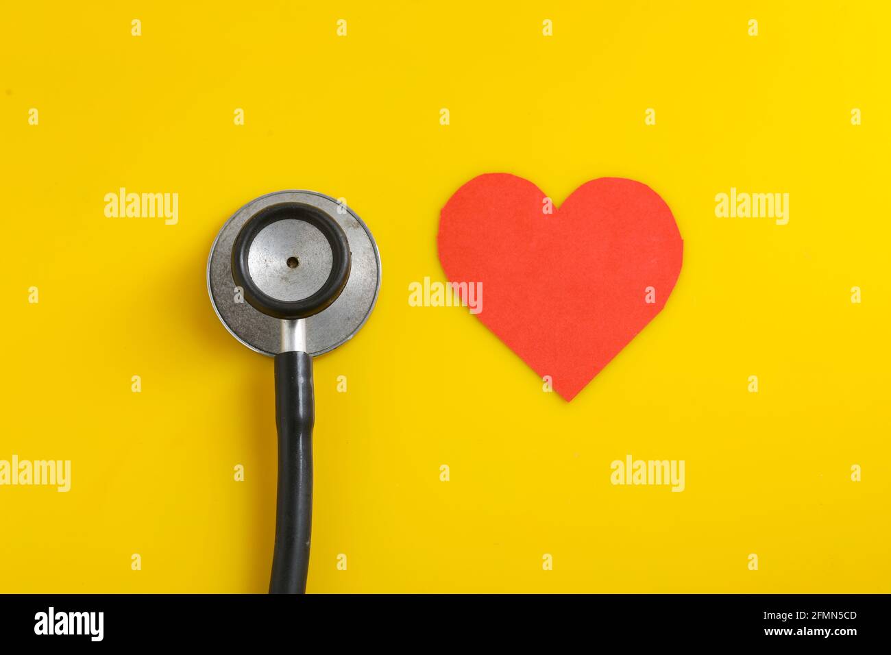 Un cuore con uno stetoscopio su sfondo giallo. Foto Stock
