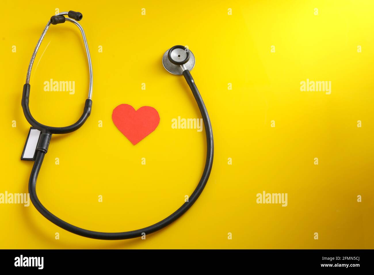 Un cuore con uno stetoscopio su sfondo giallo. Foto Stock