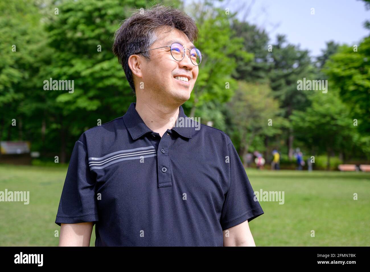 Ritratto di un uomo asiatico di mezza età che sorride sul prato indossando una T-shirt. Foto Stock