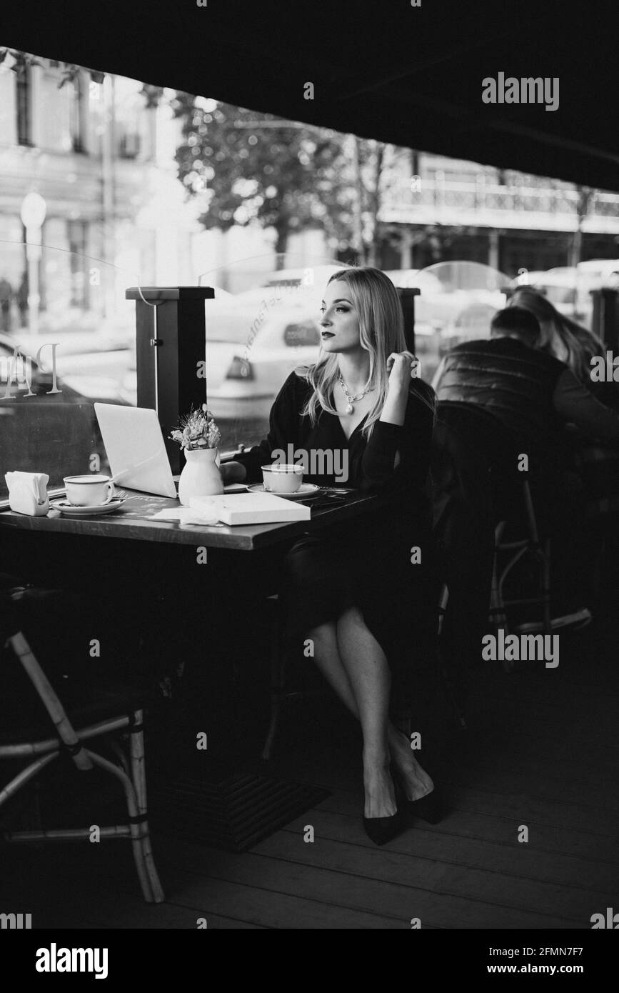 Bella giovane donna d'affari con computer portatile gode di una tazza di caffè in un caffè durante la pausa pranzo in autunno. Messa a fuoco selettiva morbida, rumore artistico. Foto Stock