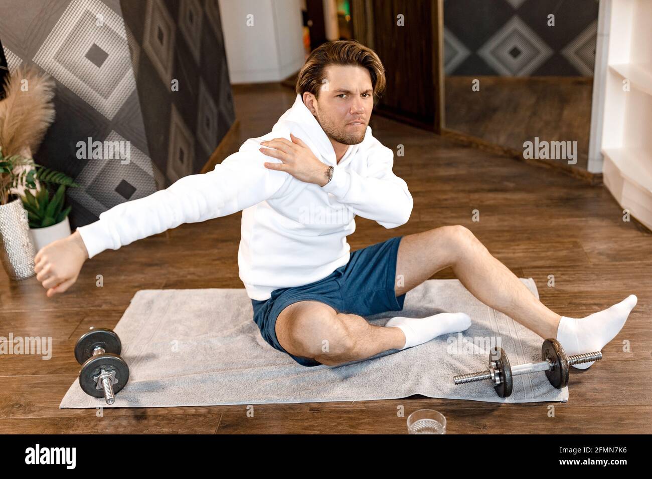 Uomo stanco ed elegante seduto sul tappetino che fa l'allenamento la mattina a casa. Bel maschio addestramento duro per mantenere l'abete del corpo e sano, motiva a. Foto Stock