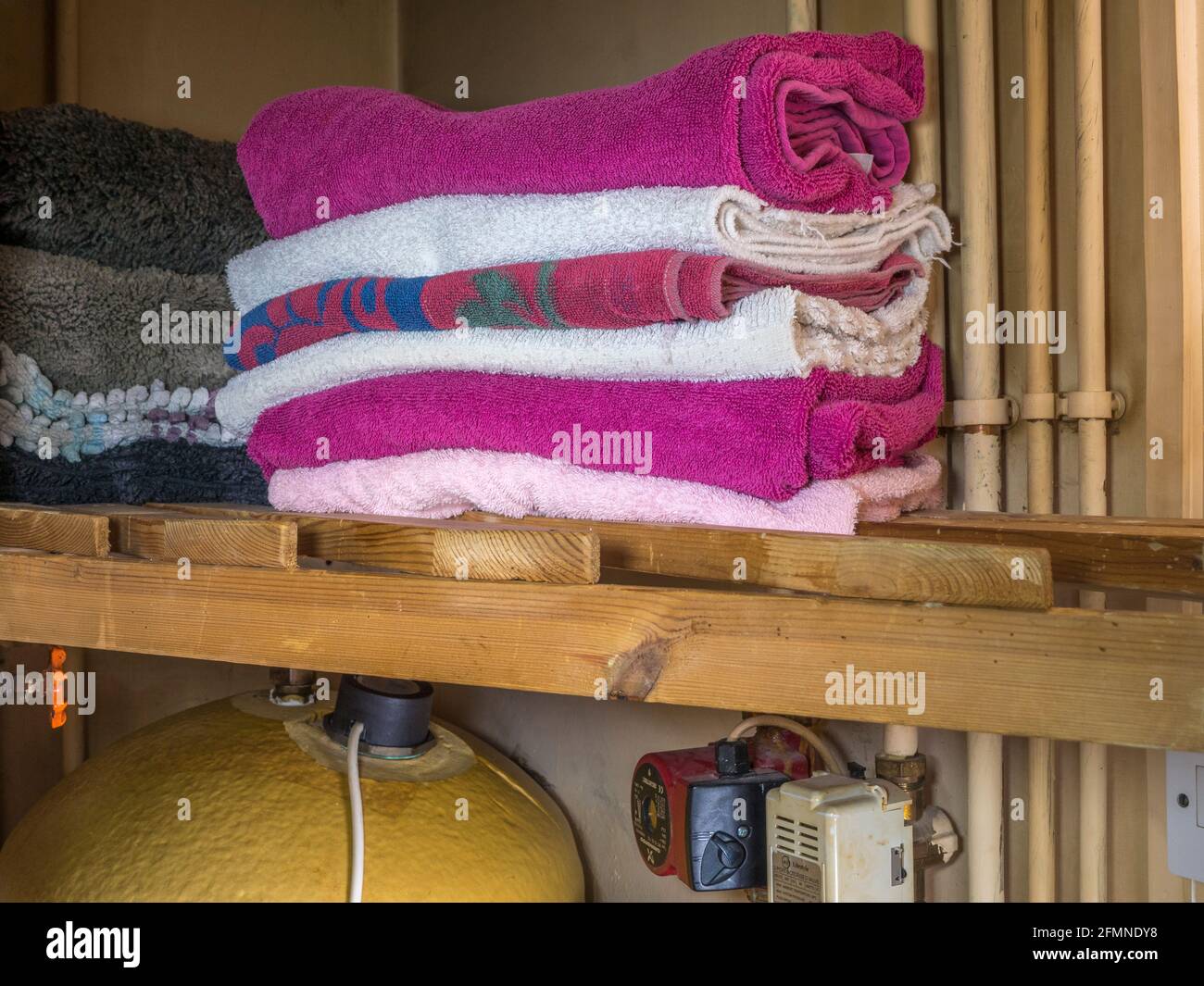 Closeup di una pila di asciugamani puliti in un armadio di aerazione, su un ripiano a doghe sopra un cilindro domestico di acqua calda. Foto Stock