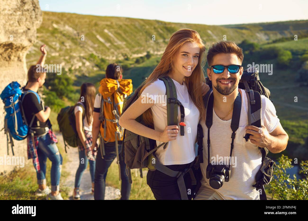 Giovane coppia sorridente escursionisti in piedi con zaini e macchina fotografica gruppo e rocce paesaggio sullo sfondo Foto Stock