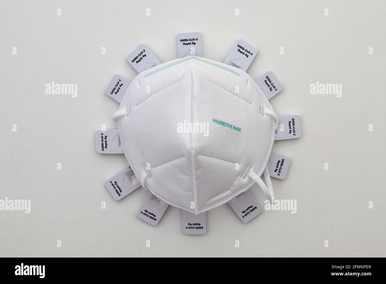 Corona virus simbolizzato da maschera facciale protettiva ffp2 e Rapid kit di auto-test antigene come proteine di punta poste su bianco sfondo Foto Stock