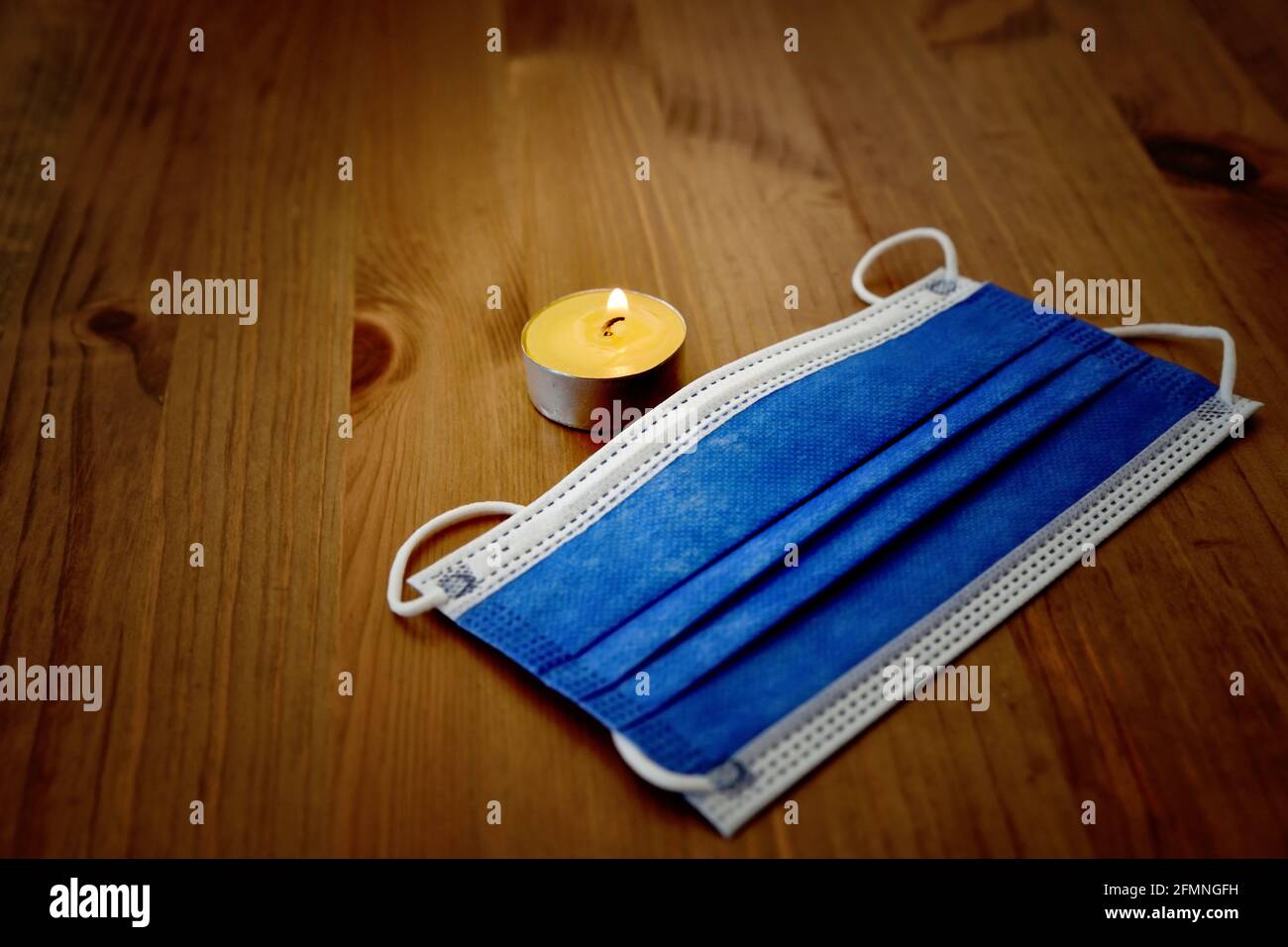 Candela bruciare per le vittime della malattia di corona virus in crisi pandemica - moody superficie di legno blu chirurgico maschera protettiva viso vignetta messa a fuoco dell'immagine attivata Foto Stock