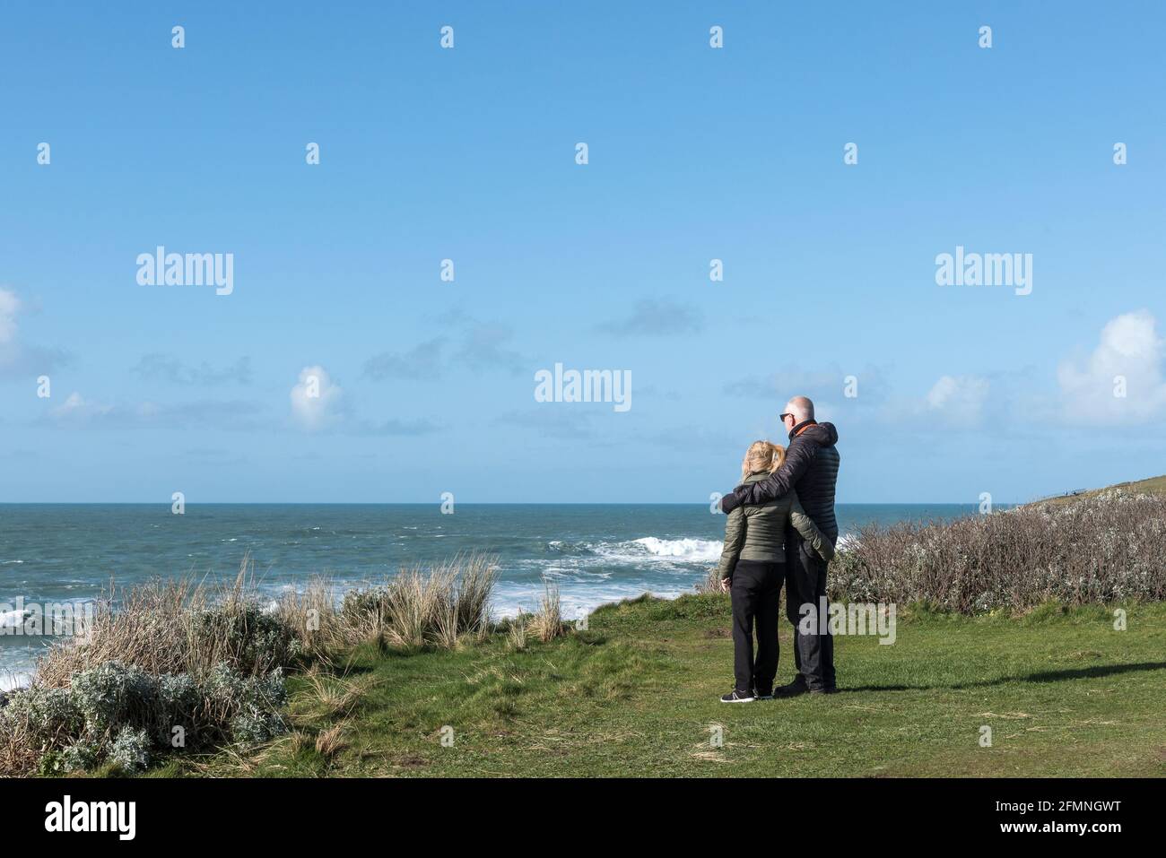 Una coppia matura con armi intorno l'una all'altra in piedi sul promontorio che guarda verso il mare a Newquay in Cornovaglia. Foto Stock