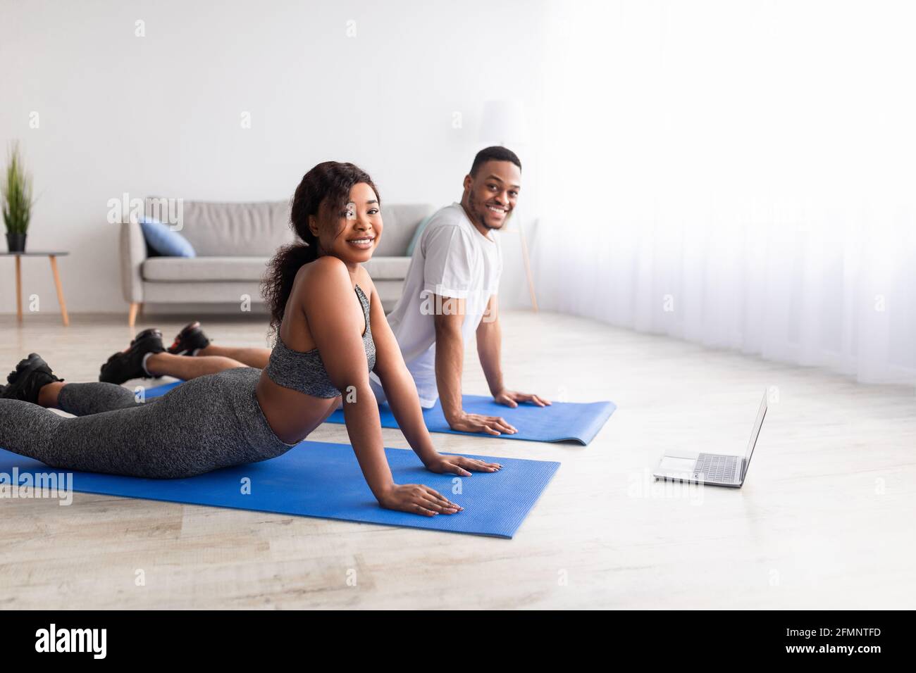 Una coppia nera sportiva che fa il backbend sui tappetini yoga, seguendo il  tutorial online sul computer portatile in interni, spazio vuoto Foto stock  - Alamy