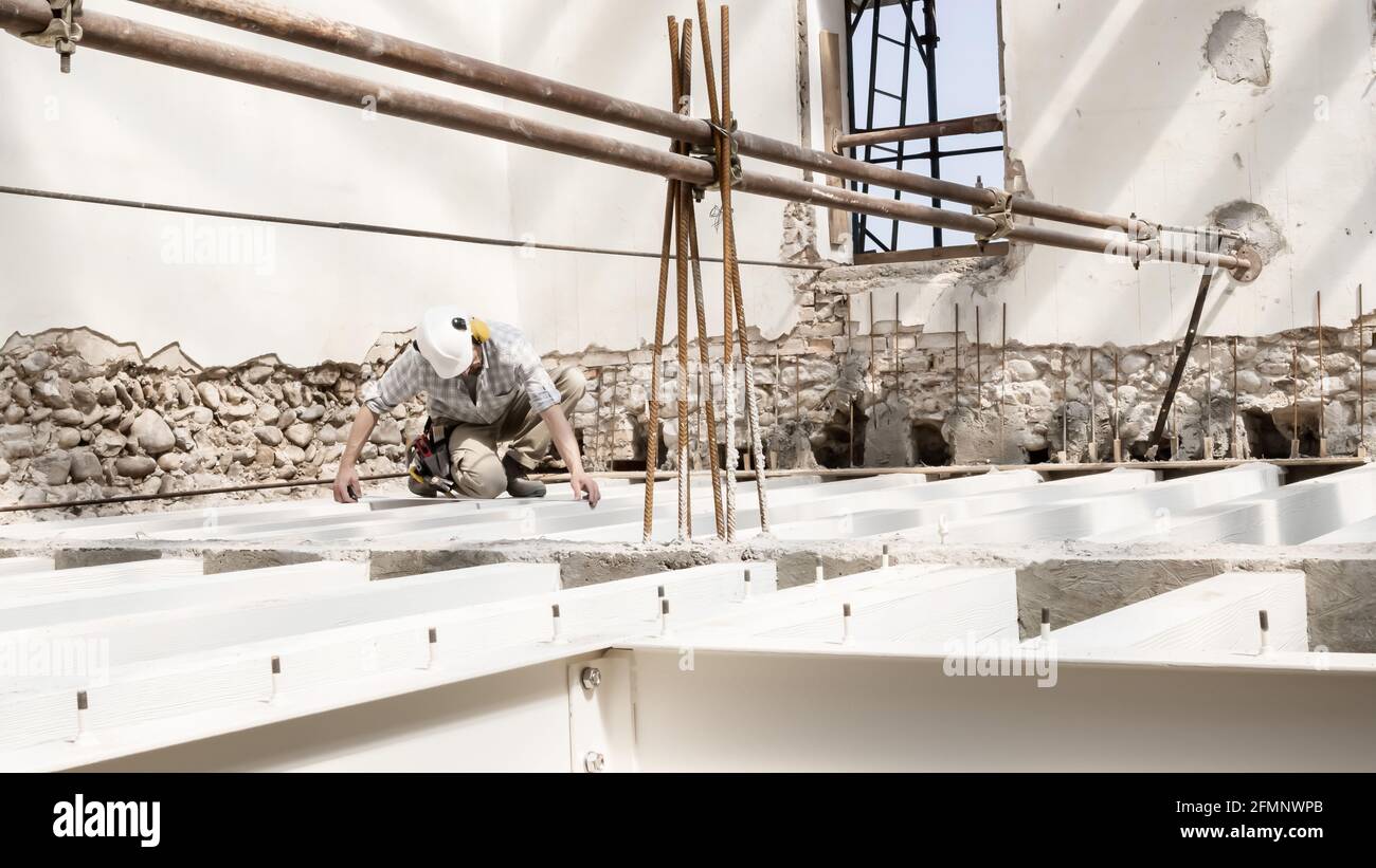 uomo al lavoro, lavoratore di costruzione indossare un casco, controllare le misure e le distanze delle travi alla base delle fondamenta del secondo piano o Foto Stock