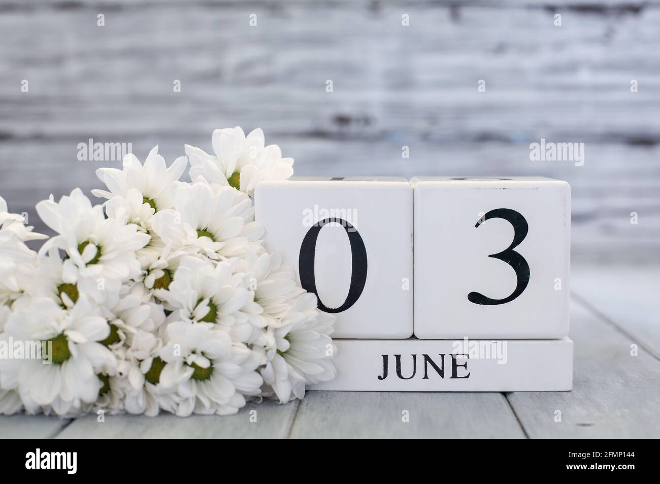 Blocchi di calendario in legno bianco con data 3 giugno e margherite bianche. Messa a fuoco selettiva con sfondo sfocato. Foto Stock
