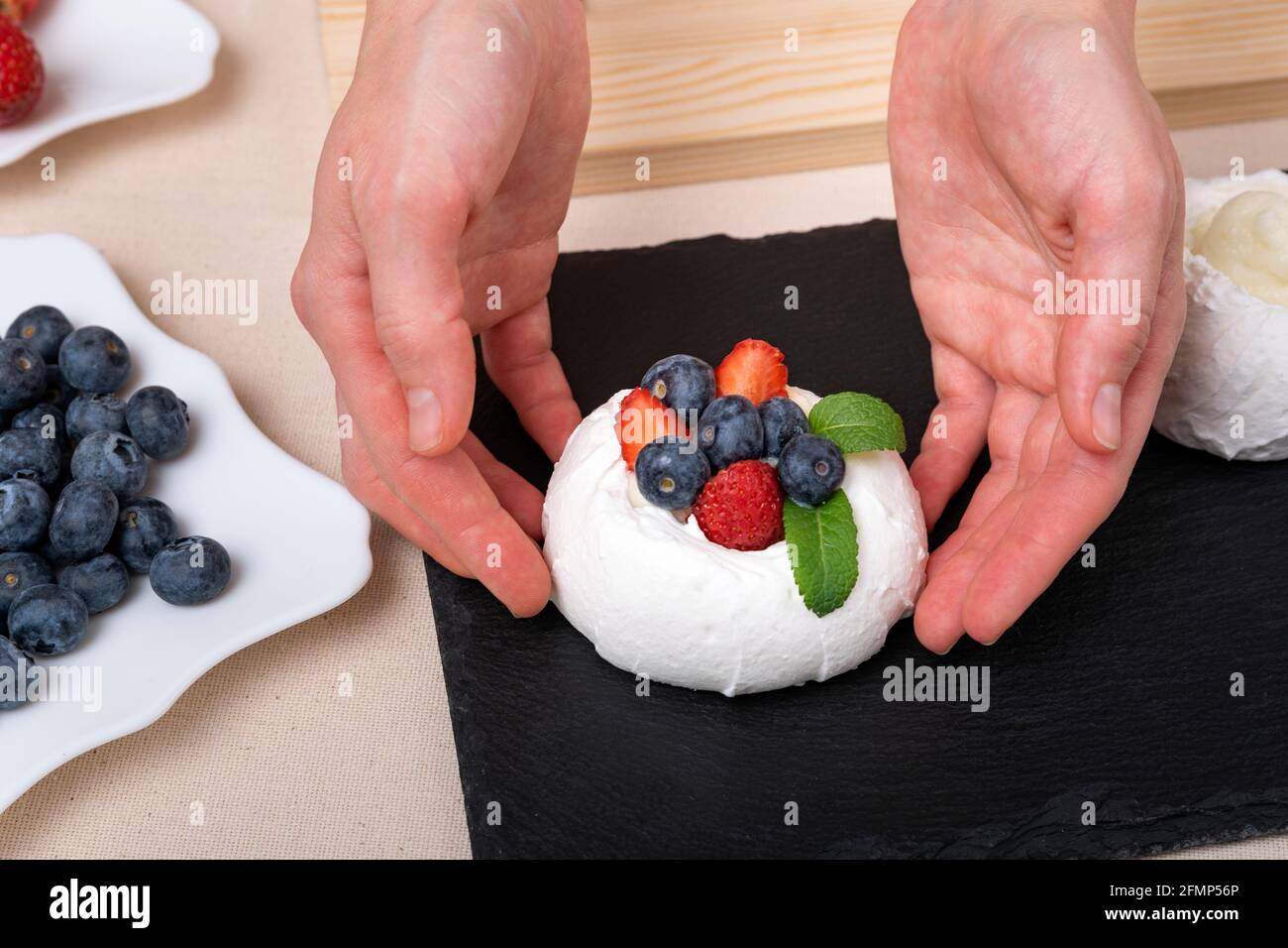 Lo chef prepara una torta delicata con frutti di bosco e menta. Torta Anna Pavlova Foto Stock