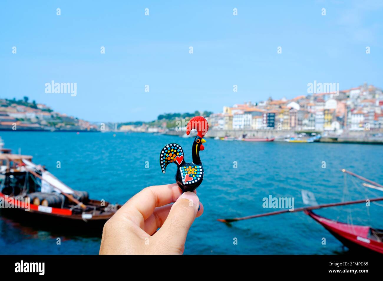 Primo piano di un giovane caucasico che tiene un tradizionale Gallo di Barcelos, l'emblema del Portogallo, a Porto, sul fiume Douro con la Disti Ribeira Foto Stock
