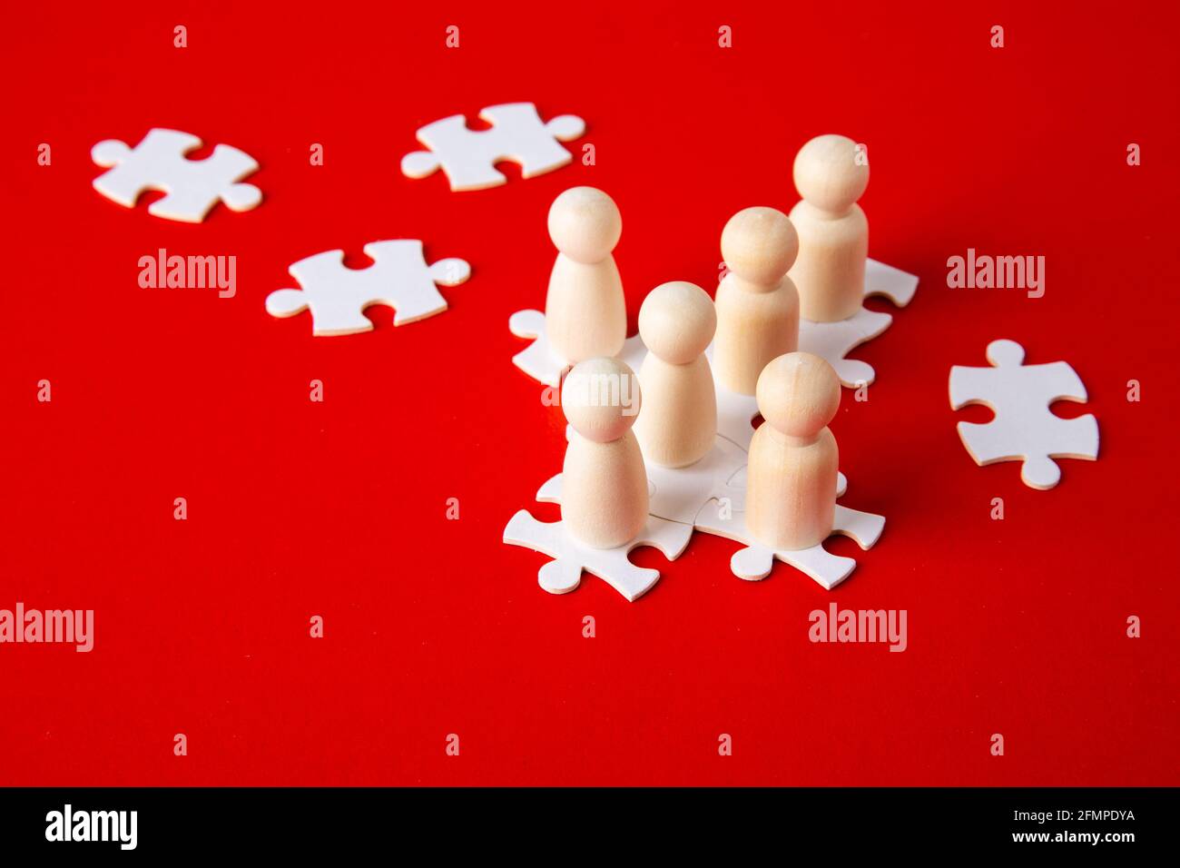 Figure di legno su puzzle su sfondo rosso come simbolo della costruzione di squadra. Gruppo di persone in affari. Cooperazione e partenariato. Foto Stock