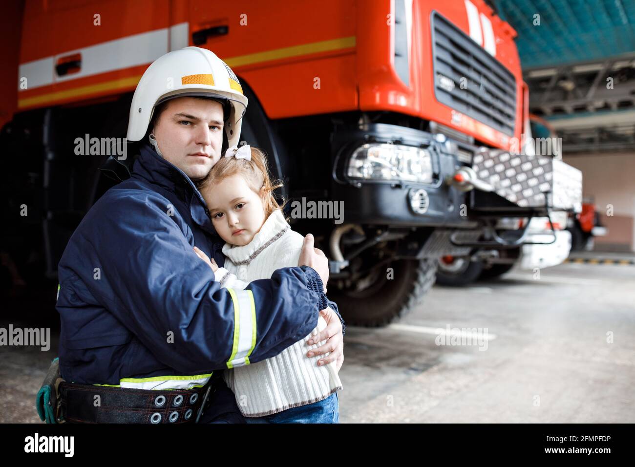Bravissimo pompiere in uniforme che tiene in piedi una bambina salvata sfondo nero Foto Stock