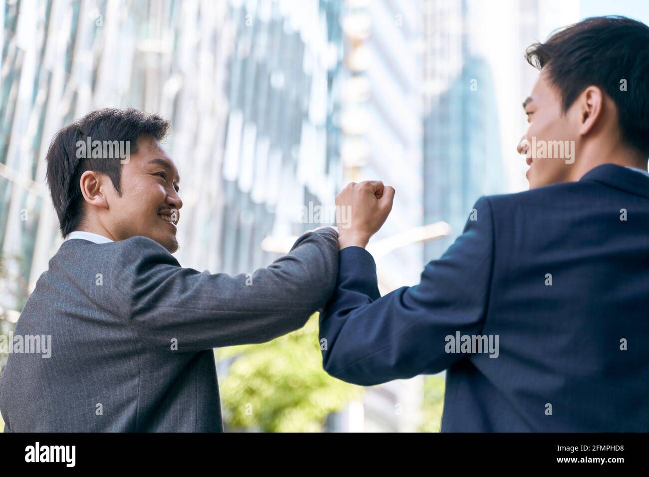 due uomini d'affari asiatici che saltano i gomiti celebrando il successo mentre camminando in strada nel cbd della città moderna Foto Stock