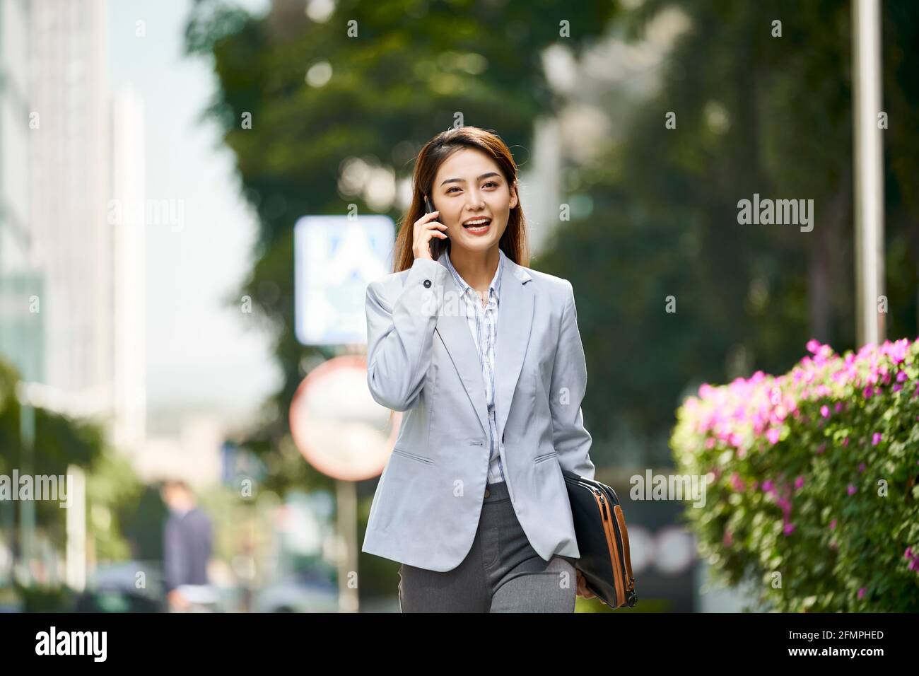 giovane donna asiatica dirigente aziendale che parla sul cellulare mentre cammina in via cittadina Foto Stock
