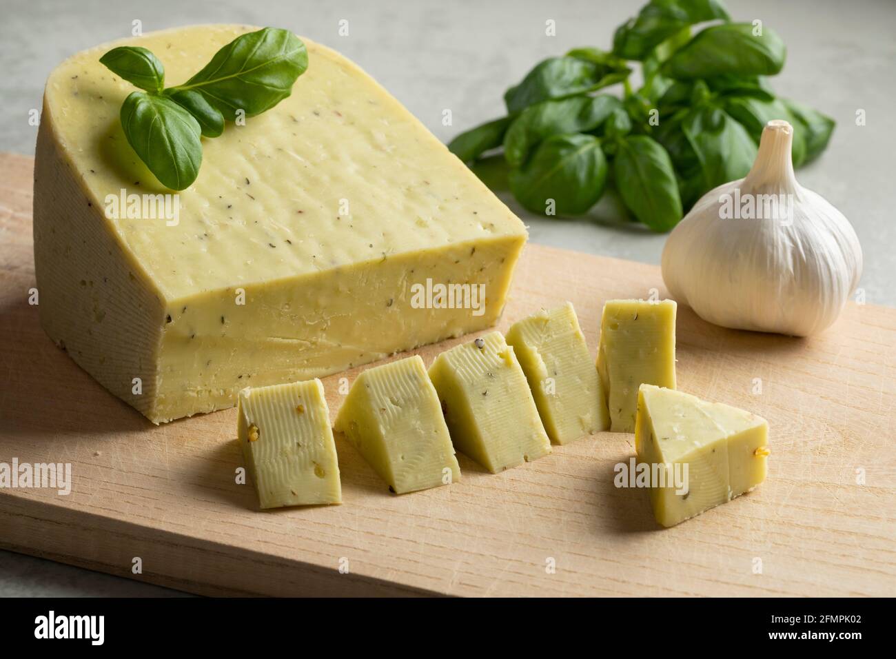 Pezzo di formaggio biologico olandese e cubetti conditi con aglio e foglie di basilico Foto Stock