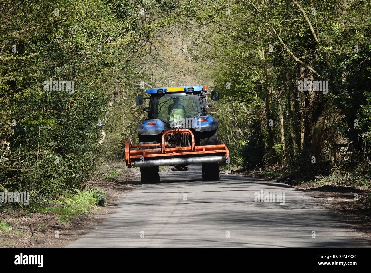 Un trattore che guida lungo una strada fiancheggiata da alberi una giornata luminosa e soleggiata Foto Stock