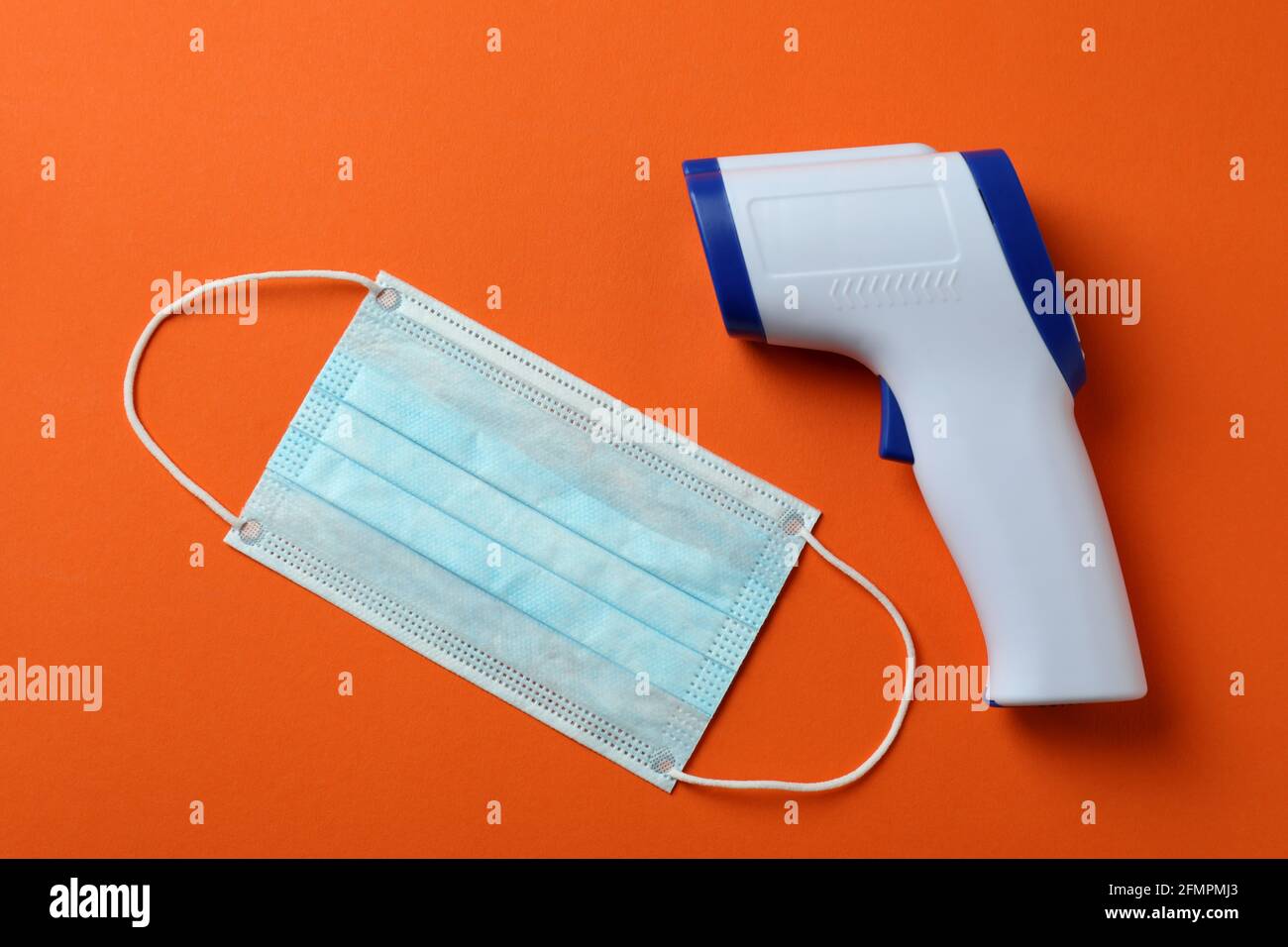 Termometro a pistola e maschera medica su sfondo arancione Foto Stock
