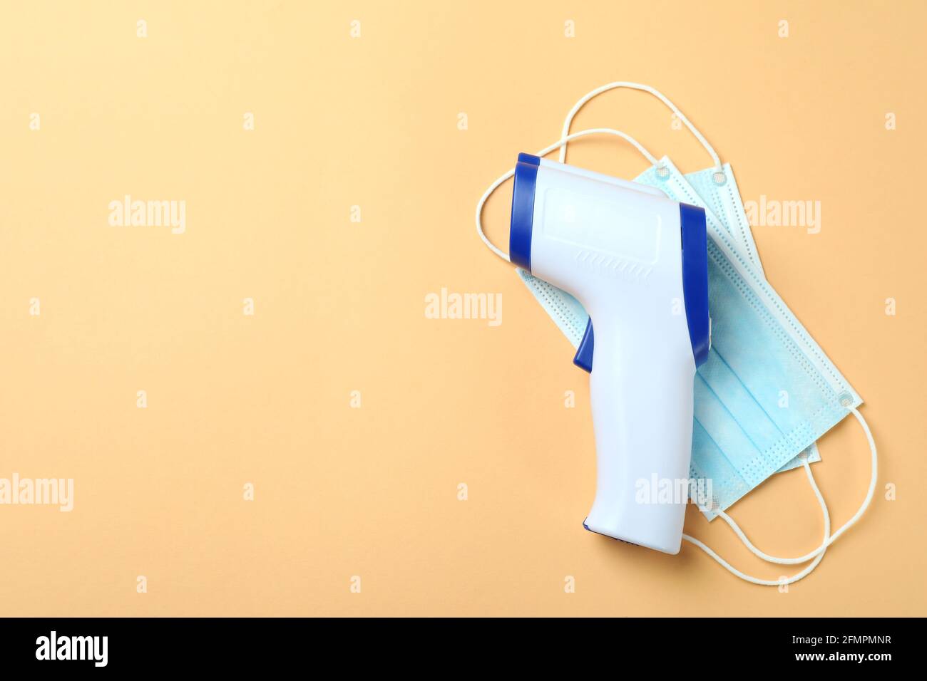 Termometro a pistola e maschere mediche su sfondo beige Foto Stock