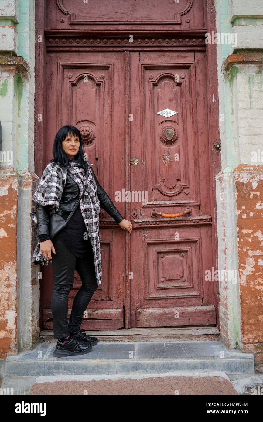 Una bella donna adulta davanti alla porta, in viaggio in Europa, vecchia porta rustica nella casa abbandonata, una persona che bussa alla porta per venire Foto Stock
