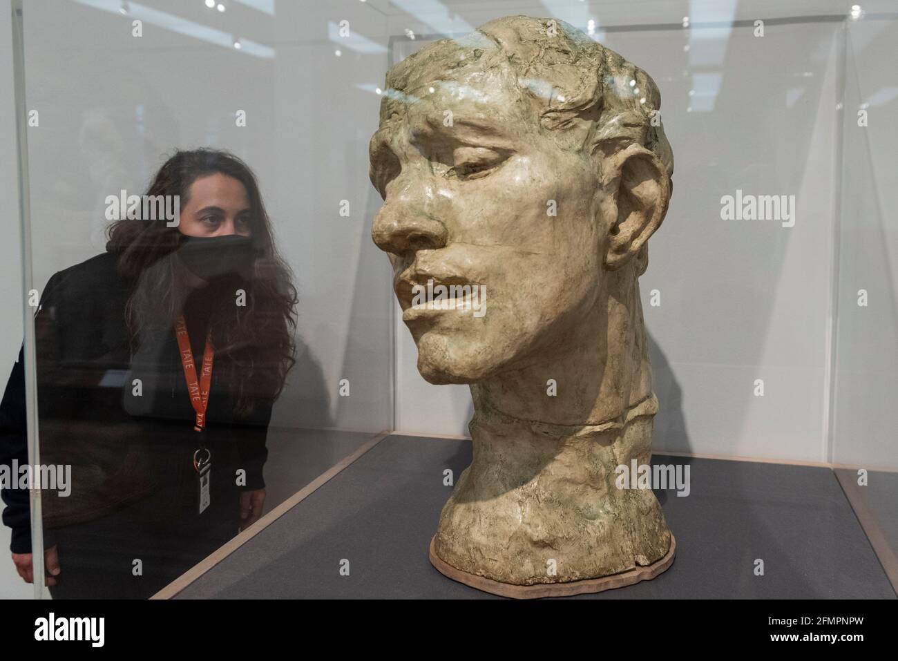 Londra, Regno Unito. 11 maggio 2021. Un membro dello staff posa con 'Pierre de Wissant, colossale Head', 1908, di Auguste Rodin. Anteprima a Tate Modern di "la realizzazione di Rodin", una nuova grande mostra di oltre 200 opere scultoree di Auguste Rodin, molte delle quali non sono mai state mostrate fuori dalla Francia. La mostra segna la riapertura del museo, in quanto il governo britannico facilita alcune restrizioni di blocco del coronavirus ed è aperta dal 18 maggio al 21 novembre. Credit: Stephen Chung / Alamy Live News Foto Stock