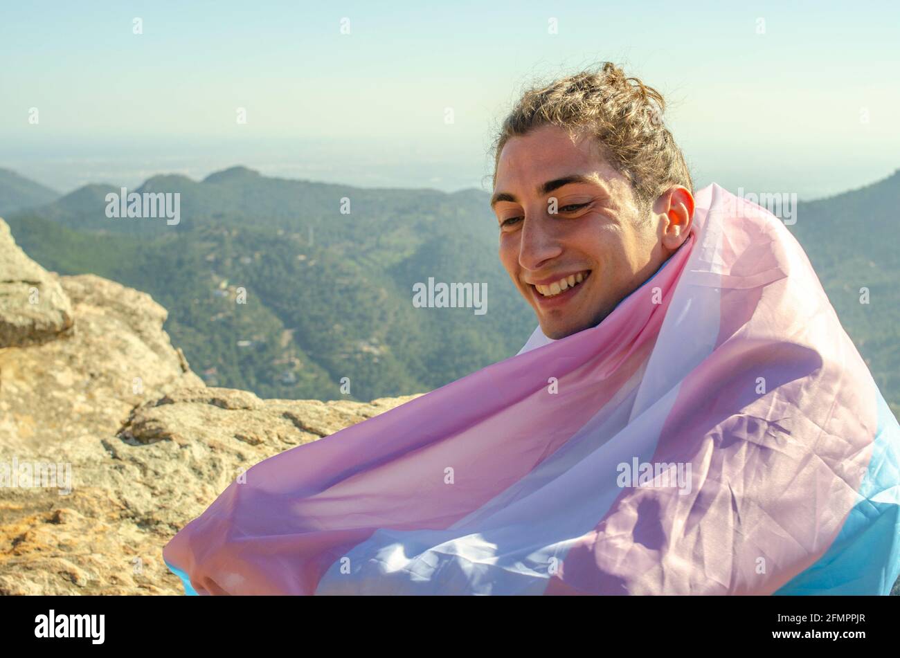 Primo piano di Handome Transgender Gay Man sorridente Cute con LGTB trans bandiera blu e rosa che lo copre Foto Stock