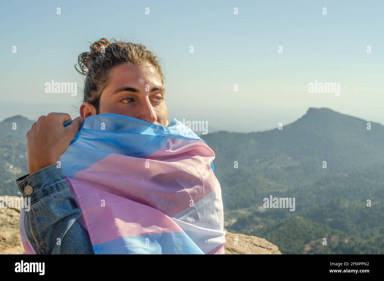Primo piano di Transgender Long Hair Man con occhi blu Coprendo il suo volto con LGTB Trans Flag Pink e. Foto Stock