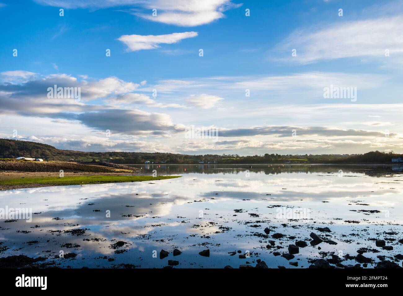Scena tranquilla con nuvole bianche nel cielo blu riflessa nel mare calmo ad alta marea in Red Wharf Bay, Isola di Anglesey, Galles, Regno Unito, Gran Bretagna Foto Stock