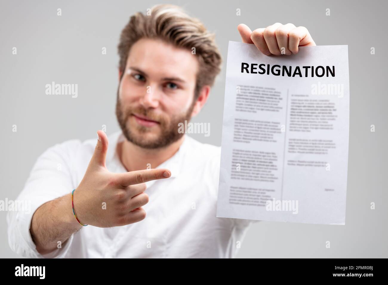 Ritratto di un giovane e felice dipendente sorridente mentre mostra la lettera di dimissioni formale dopo la decisione di lasciare il suo lavoro, in grigio con poliziotto Foto Stock