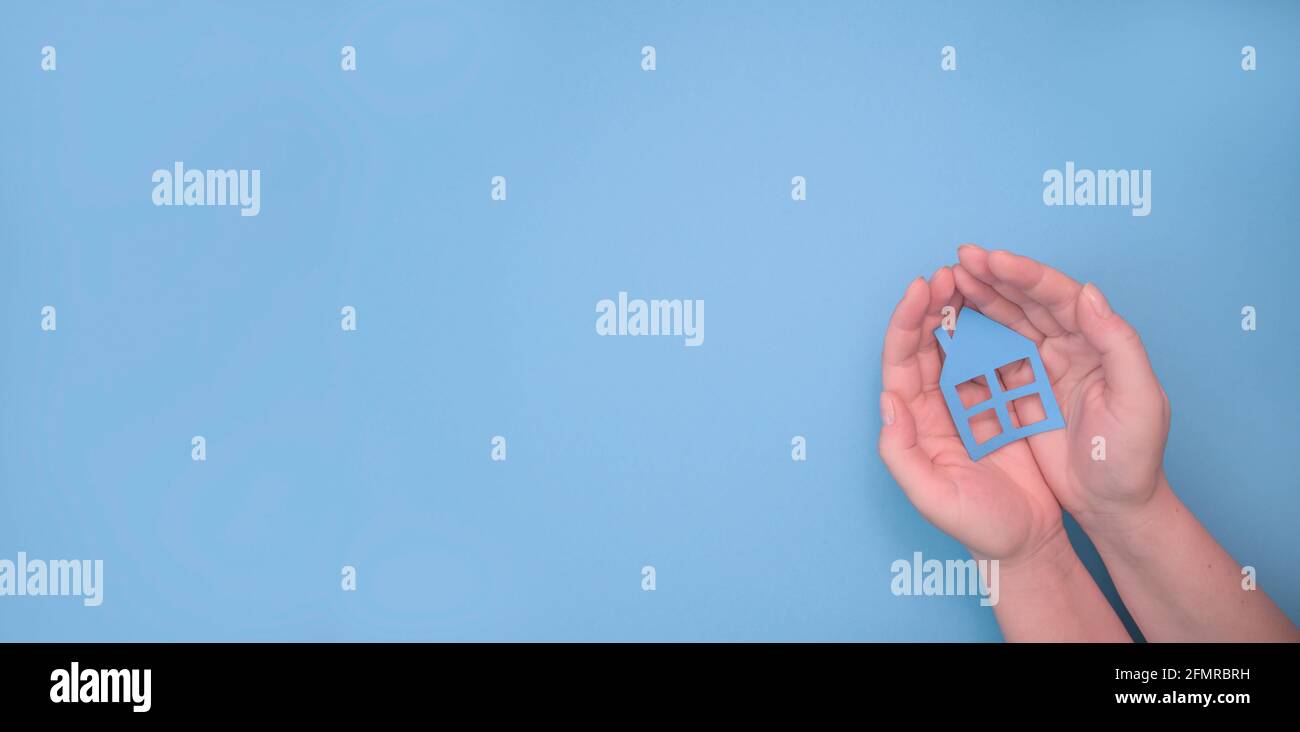 Mani che tengono la casa di carta su sfondo blu. Alloggio e casa che protegge il concetto di assicurazione, casa di famiglia, prestito di casa, assicurazione di casa, vita di famiglia come Foto Stock