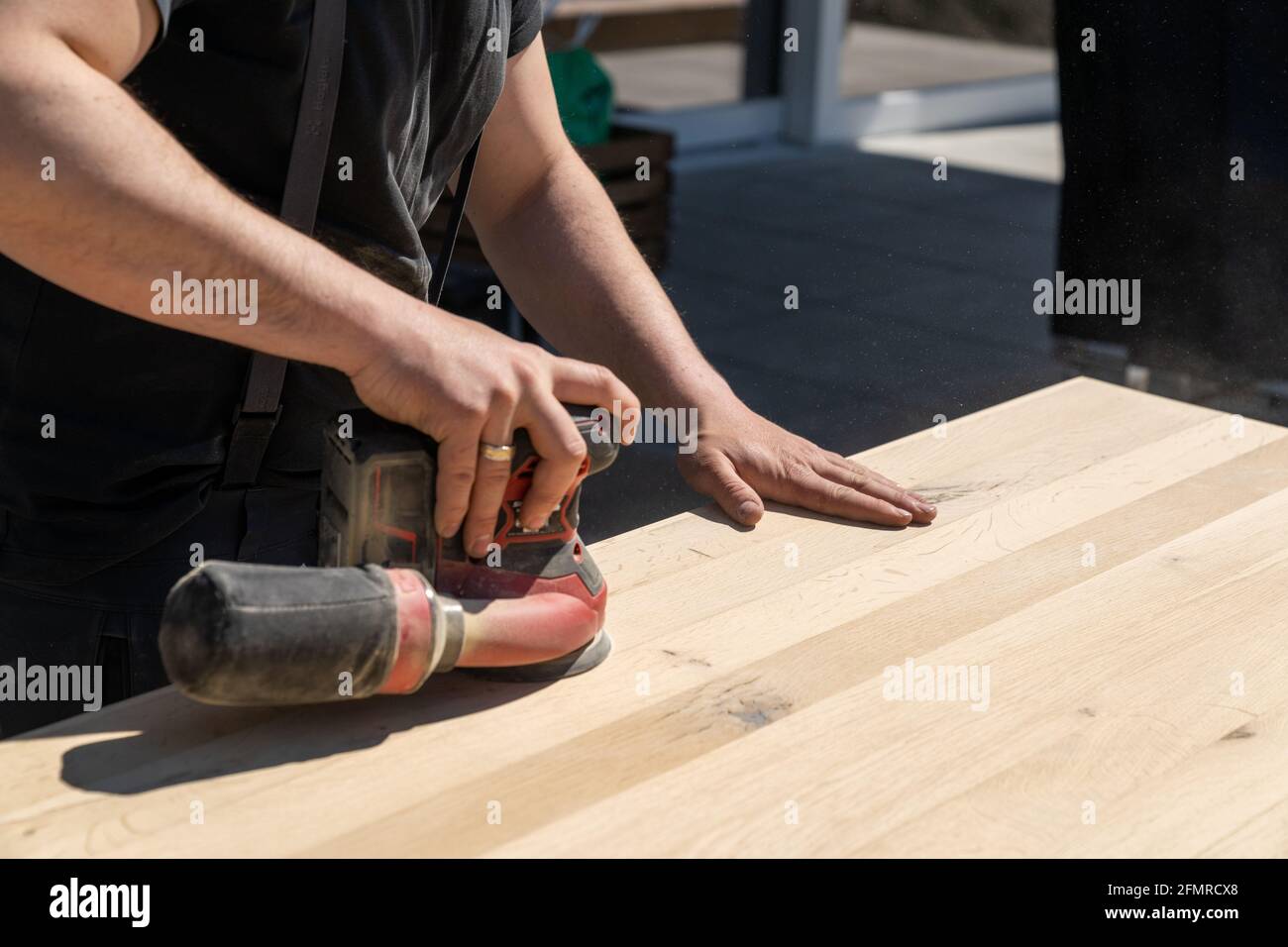 Un addetto alle costruzioni che utilizza una smerigliatrice elettrica senza fili per carteggiare un tavolo di legno massiccio Foto Stock