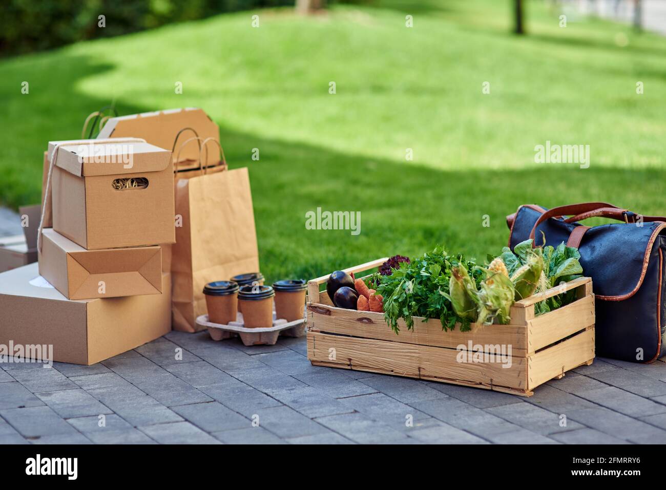 Scatola di legno con drogheria fresca, quattro tazze di caffè di carta, vari pacchetti e scatole con cibo in piedi sulla strada all'aperto Foto Stock