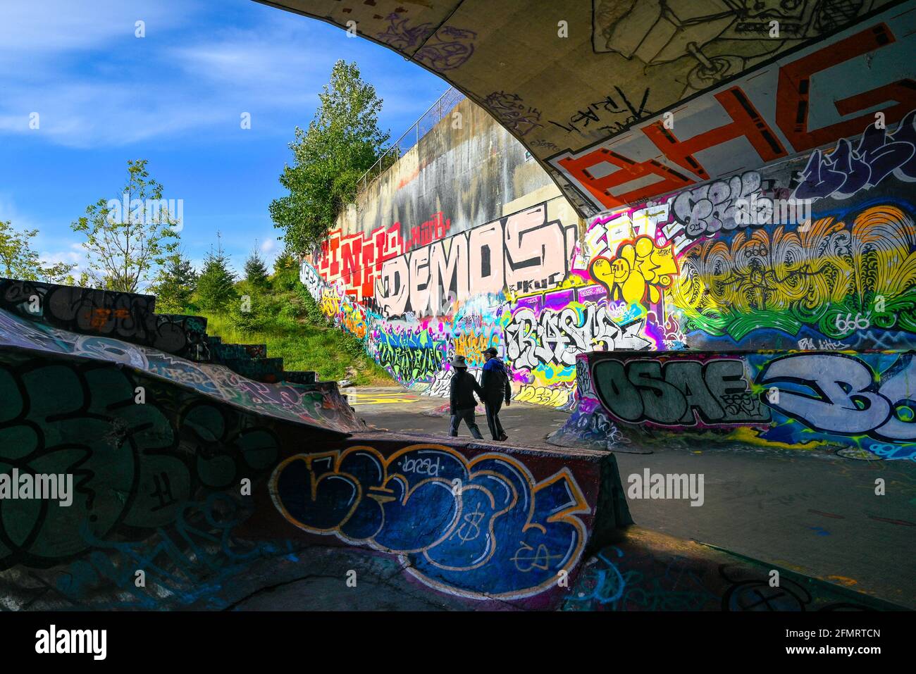 Coppia che cammina attraverso graffiti coperti, Leeside Tunnel Skateboard Park, East Vancouver, British Columbia, Canada Foto Stock