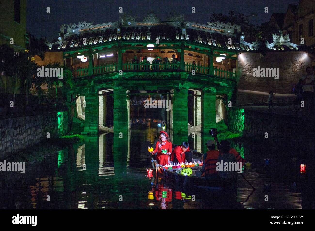 La coppia vietnamita sedette in barca di fronte al ponte giapponese rilasciare lanterne galleggianti colorati nel fiume, Hoi An, Vietnam Foto Stock