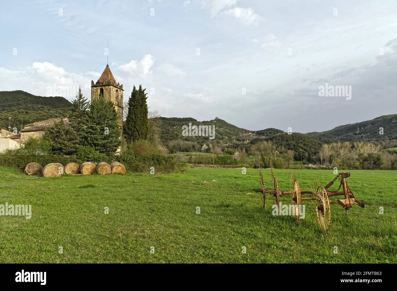 Tipica campagna catalana, erba rurale con il vostro rasaerba, waltz paglia e la chiesa, circondata da montagne. Foto Stock