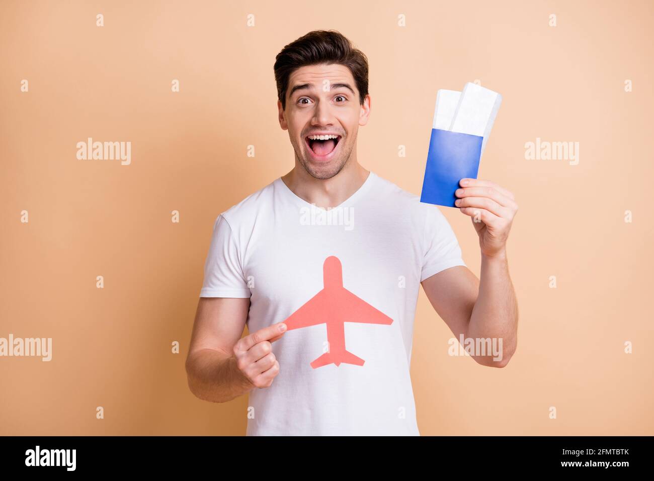 Foto di ottimista brunet uomo stand tenere aerei biglietti usura t-shirt bianca isolata su sfondo di colore beige Foto Stock
