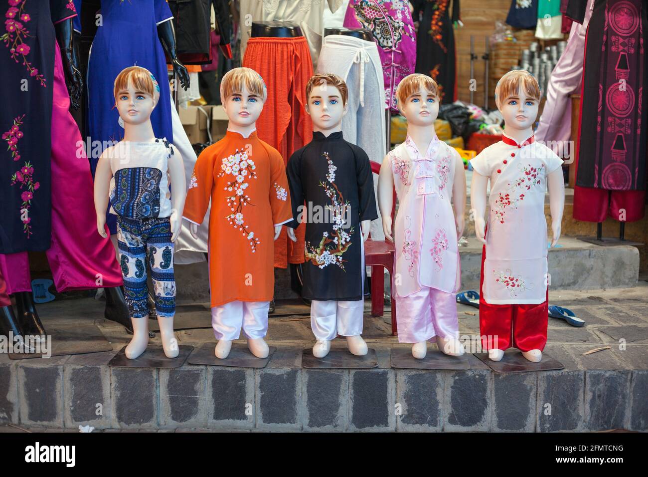 Abiti tradizionali vietnamiti Ao dai indossati da manichini per bambini fuori negozio nella città vecchia, Hoi An, Vietnam Foto Stock