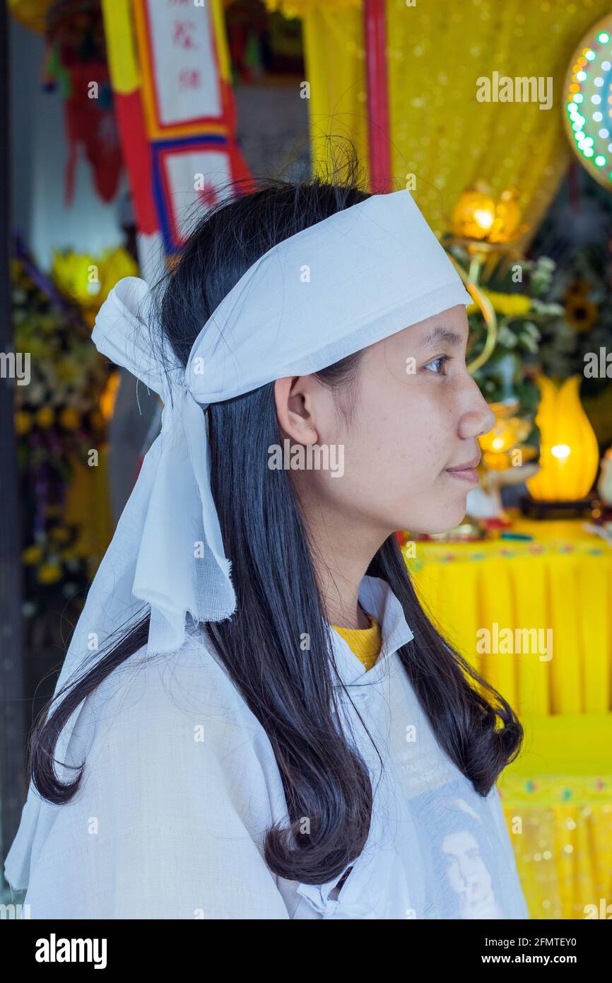 Profilo di giovane attraente donna vietnamita vestita in bianco che partecipa al servizio commemorativo per nonna che era morto di recente, Hoi An, Vietnam Foto Stock