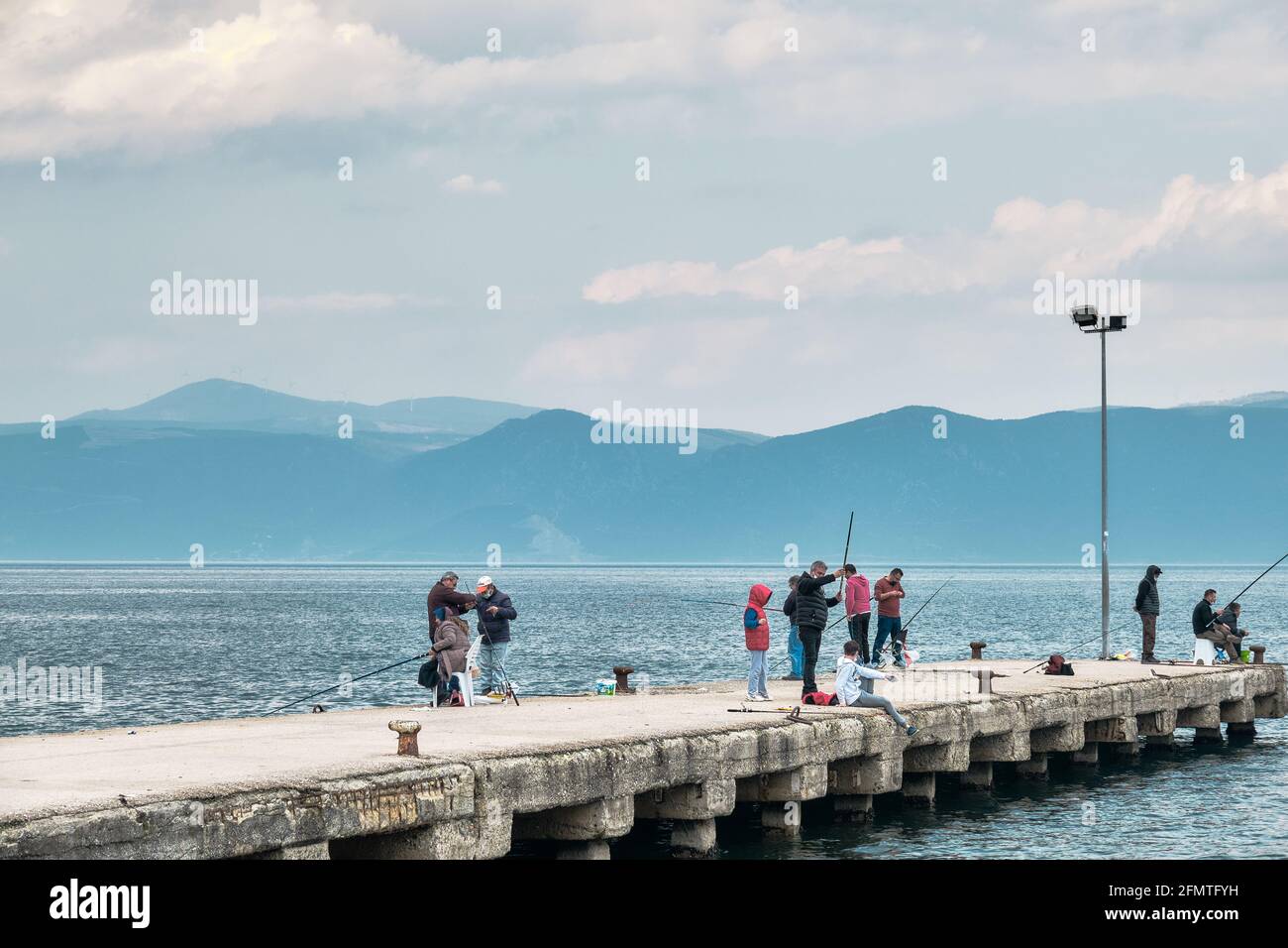 Molte persone che pescano sul molo e il porto si estende al mare di marmara durante il tempo sovrastato e la giornata delle piogge. Sole che arriva dopo le nuvole. Foto Stock