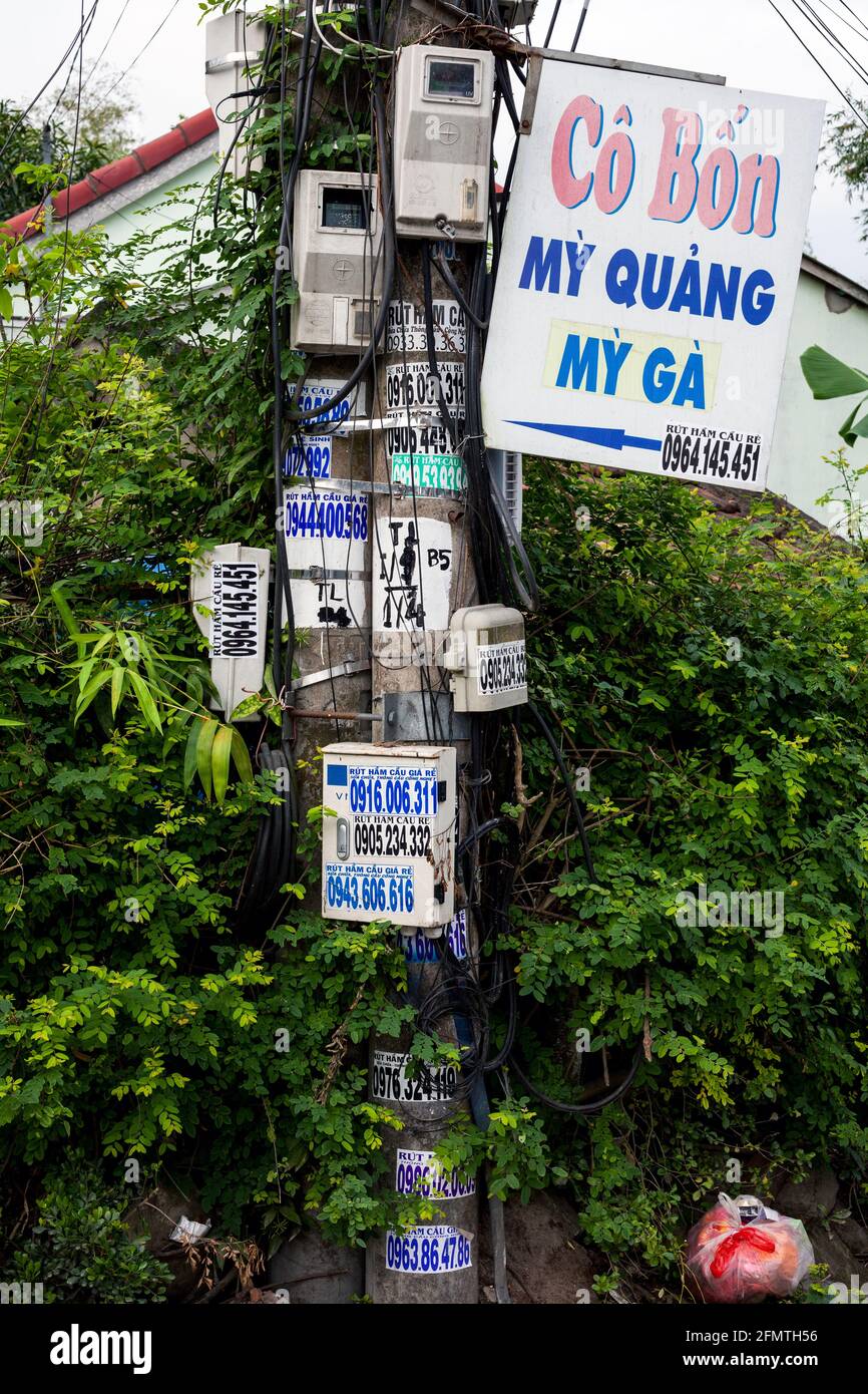 Palo stradale contenente fili, metri, numeri e direzioni, Hoi An, Vietnam Foto Stock