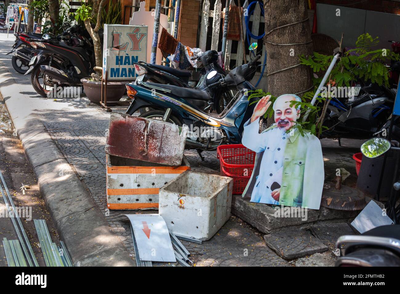 Il cartone tagliato fuori di ho Chi Minh ondeggiando sedette sul marciapiede che giace tra gli articoli scartati, Hoi An, Vietnam Foto Stock