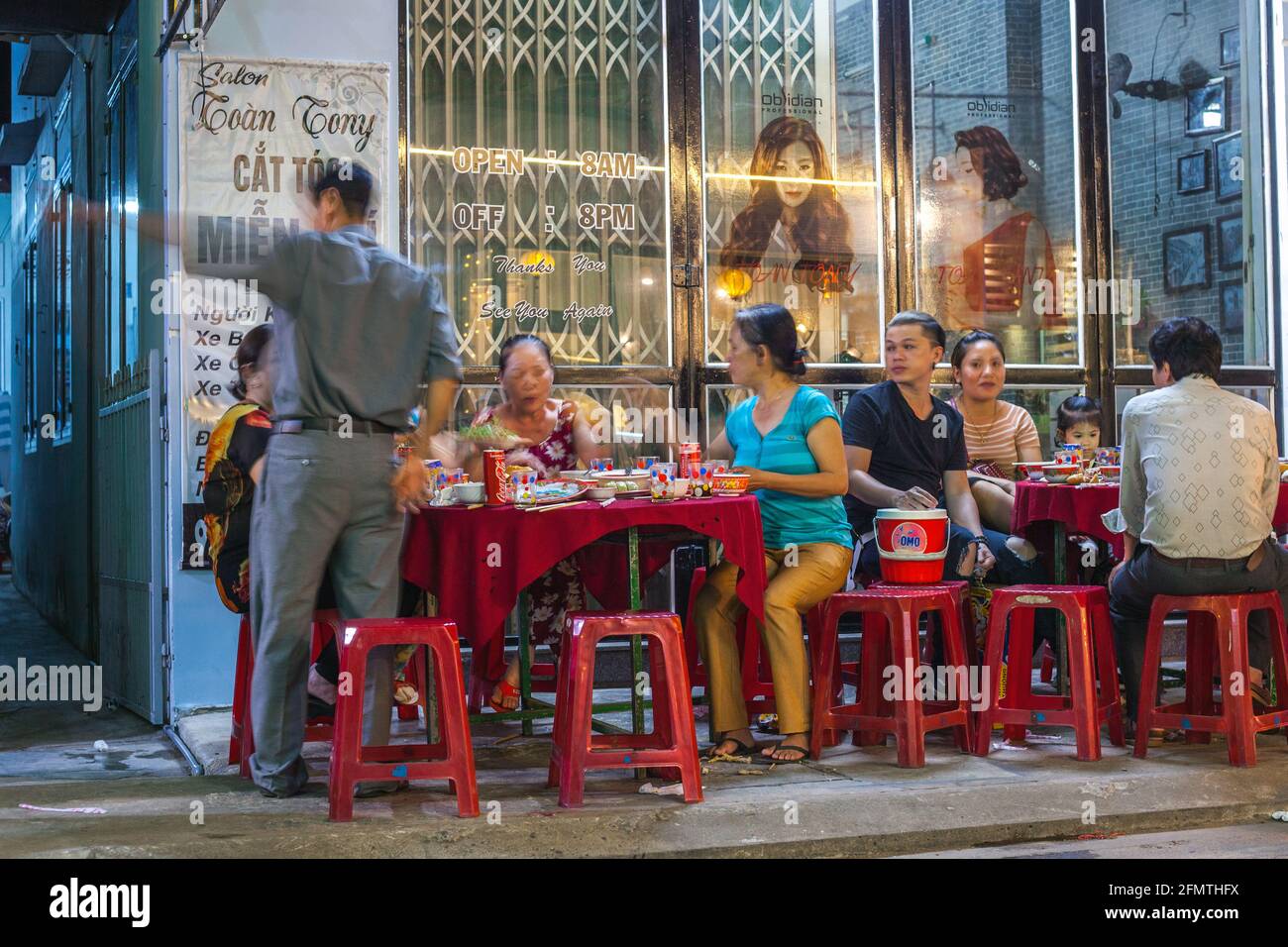 Le famiglie vietnamite seduti al caffè all'esterno del parrucchiere, Hoi An, Vietnam Foto Stock